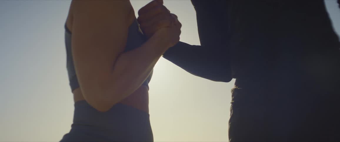 A young fit couple perform a handshake in front of the sun
