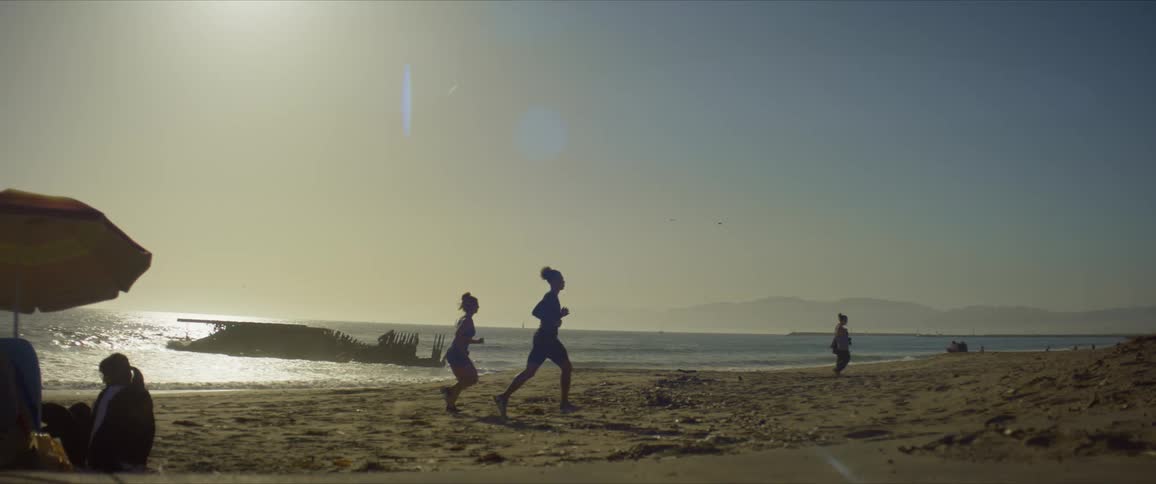 Beach scene with sunbathers sitting walking and a couple running in the sand