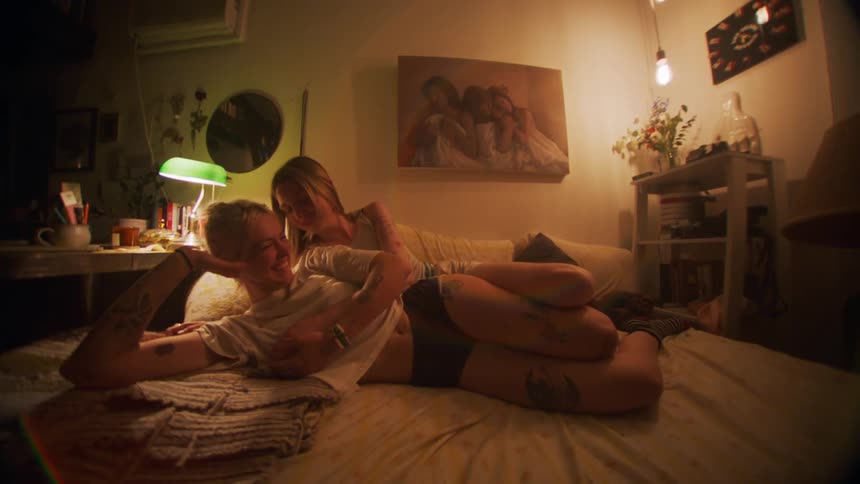 Two women lying embraced in bed talking and smiling affectionately