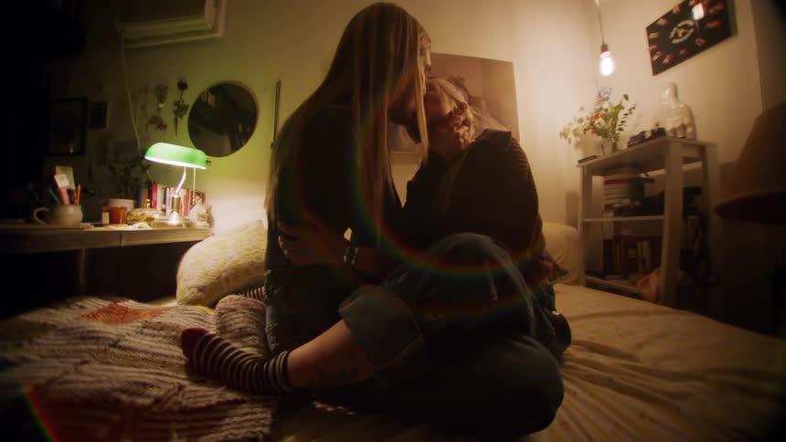 Two women sitting on top of each other in bed kissing warmly
