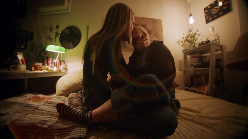 Two women make out while sitting in a bed
