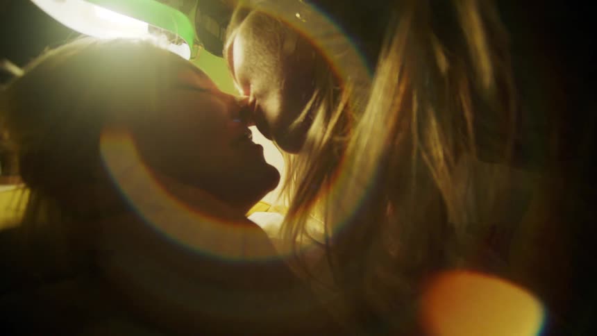 A happy lesbian couple makes out on the bed under the lamp light