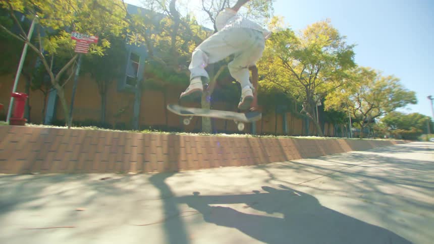 A black teenager jumps with and steps off of a skateboard on a sidewalk