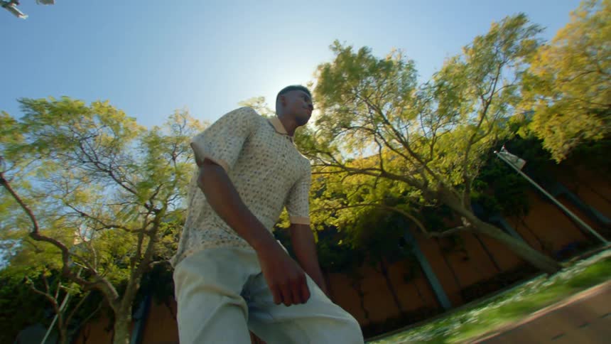 Man riding a skateboard on a sidewalk in a city with trees beside him
