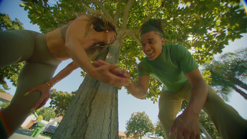A man and a woman slap hands smile while standing under a tree