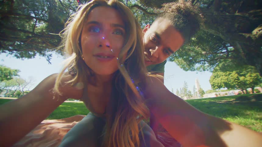 Woman sitting on a towel on the grass in a field and a man behind helping her stretch her body