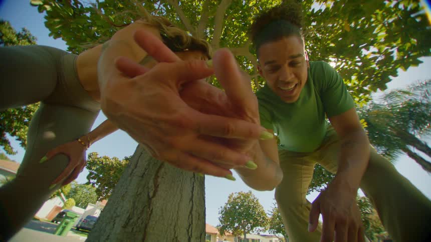 Woman with her hand outstretched and the man next to her clapping hers while they are under a tree