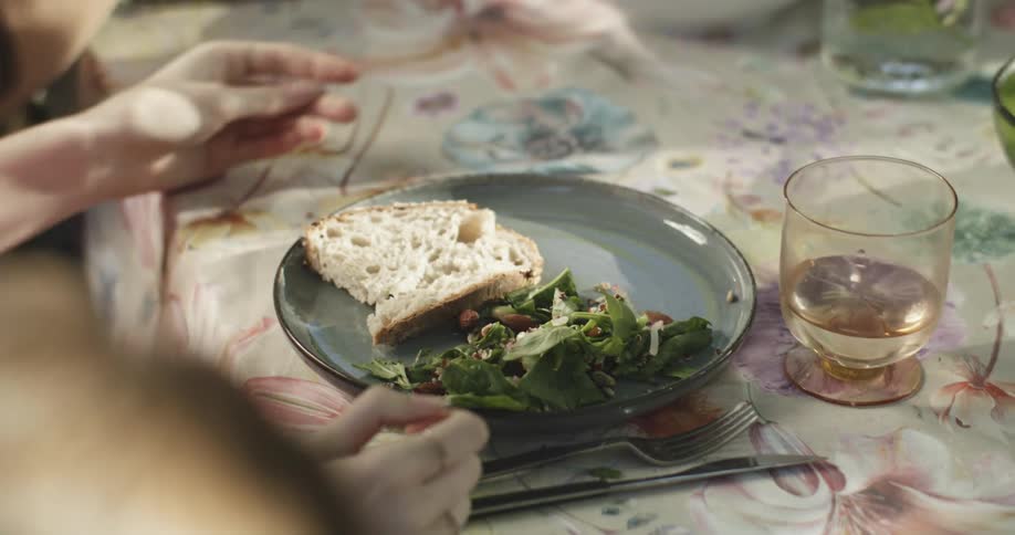 Woman taking a bowl with a slice of bread placing it on her plate and eating it with vegetables
