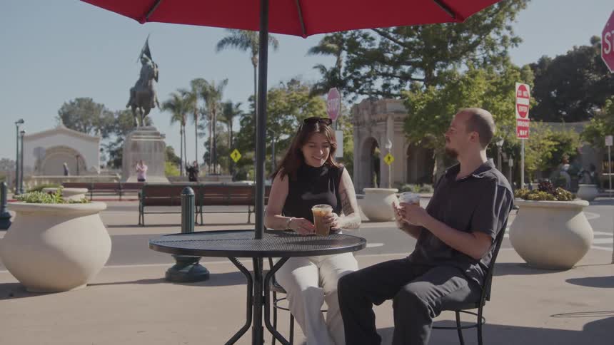 A couple enjoy beverages near old buildings and a statue