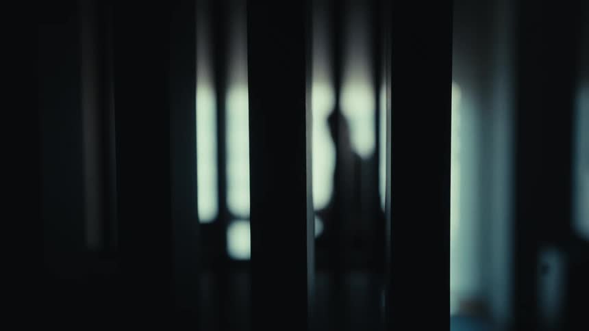 An out of focus silhouette of a person moving behind bars in a dimly lit room