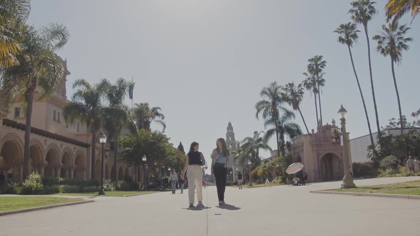 Female friends walk along wide path between buildings with multiple arches