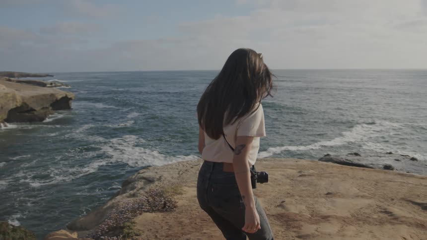 Woman walking on rocky shore on seaside cliff during daytime