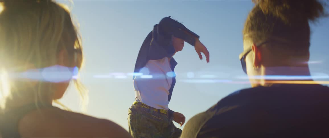 A man and woman both wearing sunglasses and black tops watch a dancer perform with sunlight in the background