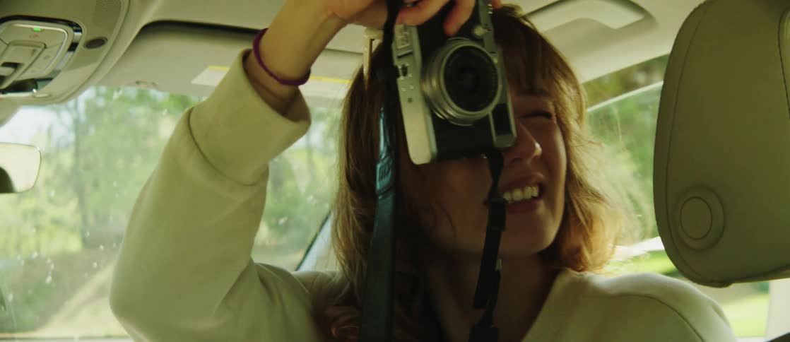 Young woman in the front seat of the car with a vintage camera photographing