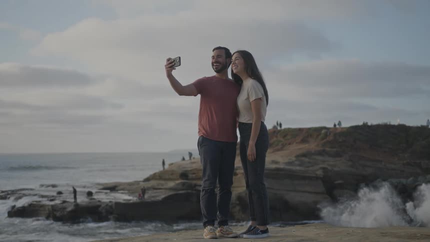 A couple walk on the beach and take a photo with their cell phone
