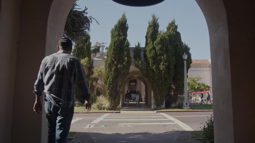 An older man walks through an arched doorway that leads to a street