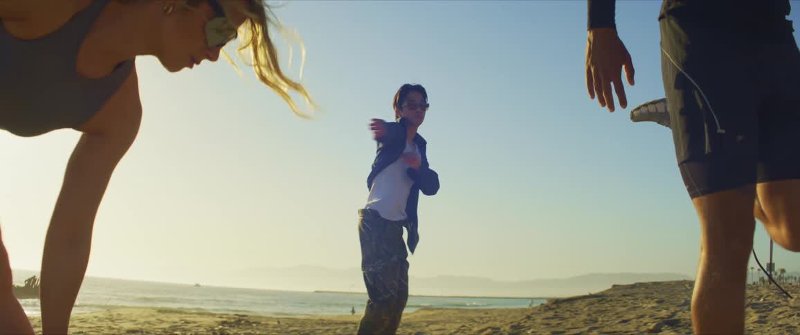 Man dancing on the beach sand and next to him two people stretching
