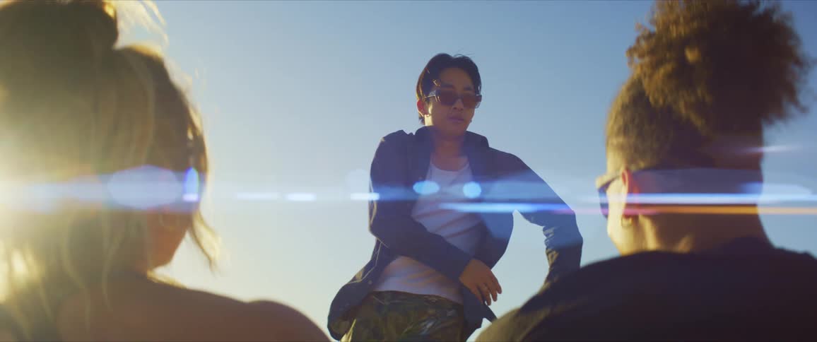 Two friends looking towards a man dancing under a bright sky
