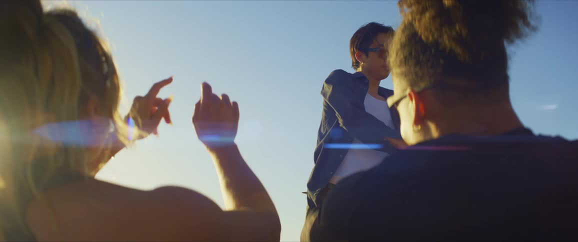Man standing dancing in an openair place and two other people watching and cheering together with their hands