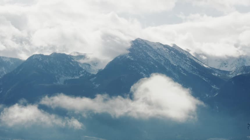 A mountain range with peaks partially covered by snow and enveloped in clouds