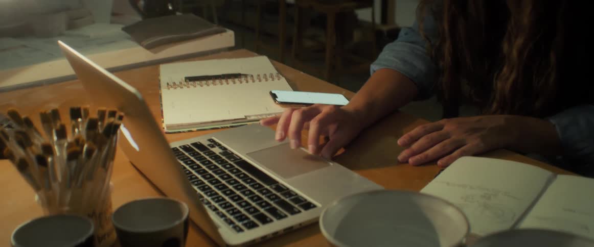 An attentive woman wearing a blue shirt working on her laptop at a desk in a workshop