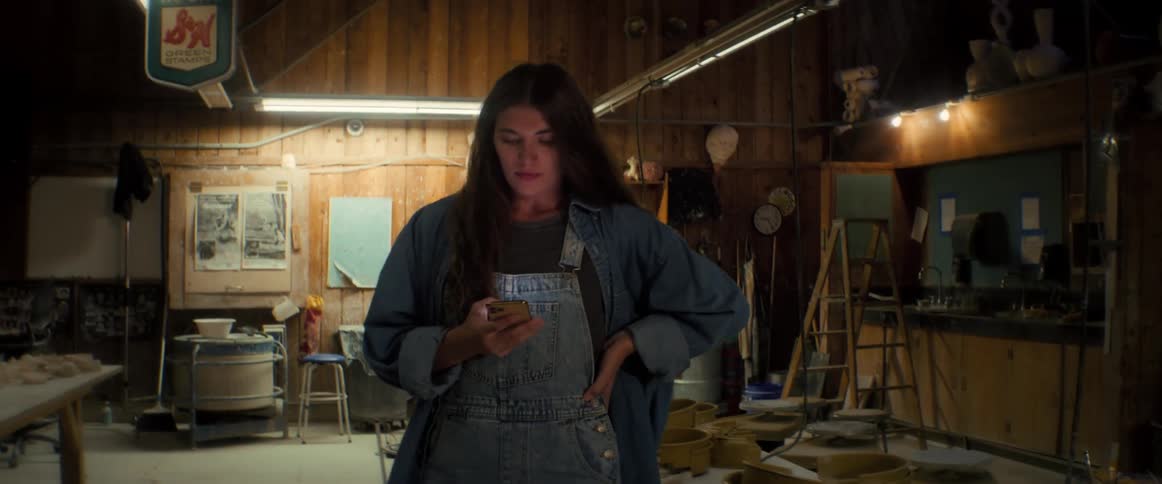 A potter paces back and forth in her workshop at night while looking at her phone