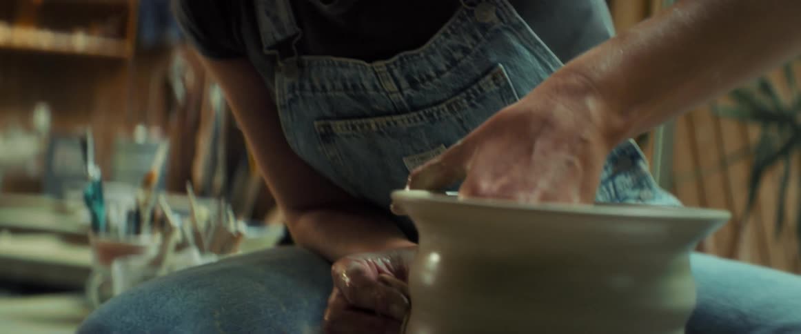 A smiling woman shapes clay on a pottery wheel