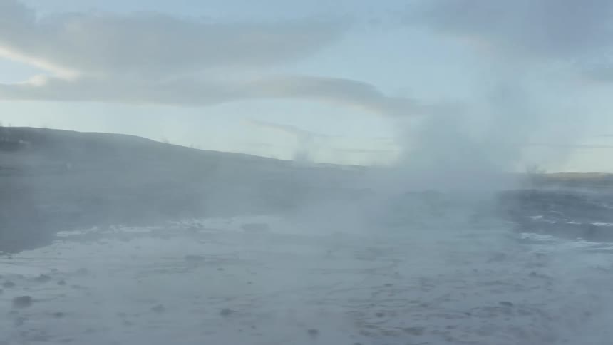 A landscape with geothermal activity steam rising from the ground against a clear sky