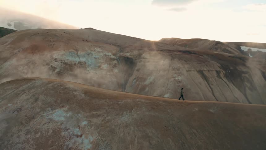 Man hikes along mountain top during winter under a red tinted sky