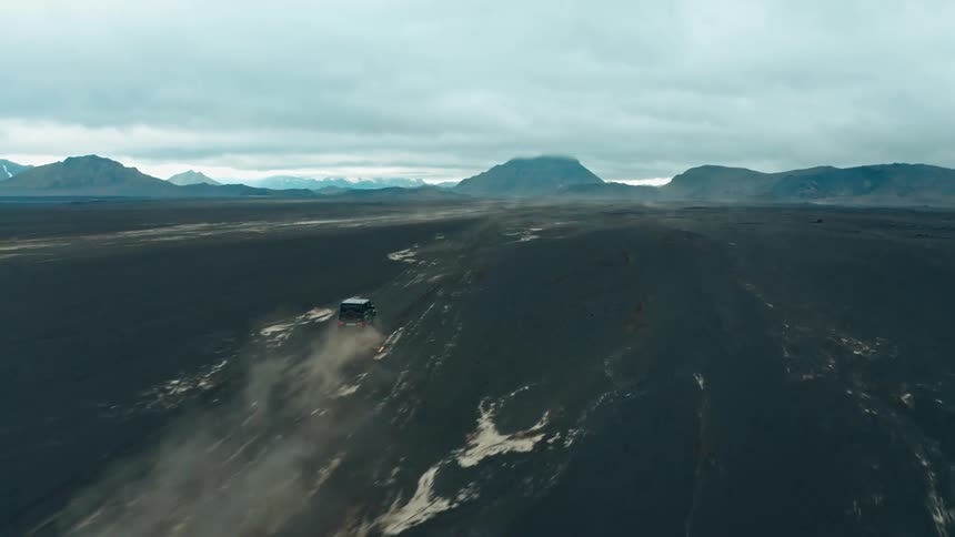 Aerial panorama of a black jeep traveling on black ground with mountains on the horizon