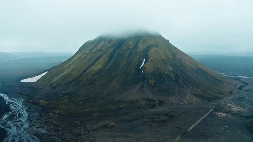 An aerial view of a solitary mountain surrounded by a rugged landscape and a river
