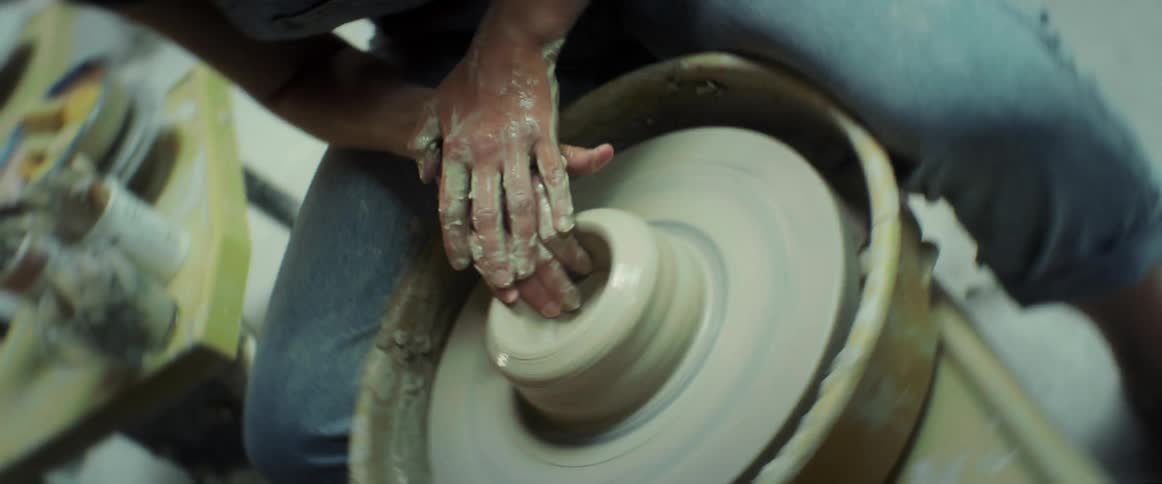 A woman wearing jeans shaping a lump of clay on a pottery wheel