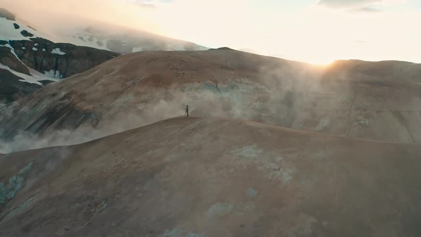 A person stands on a mountaintop gazing out at a vast landscape of snowcapped peaks