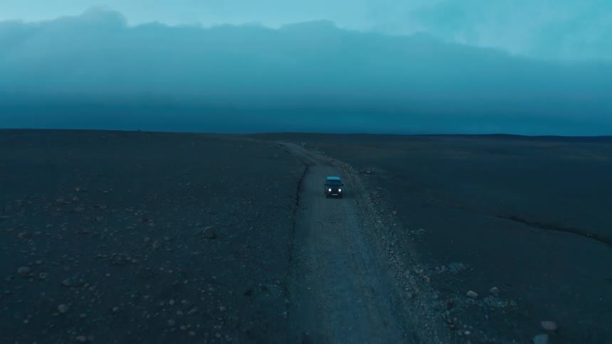 A vehicle with headlights on driving along a narrow dirt road