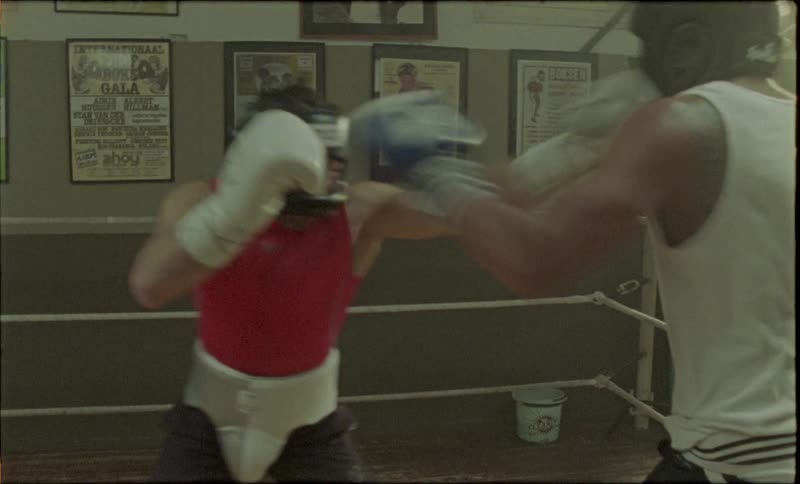Two men wearing boxing gloves and headgear are training in an indoor gym