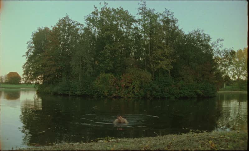A man emerges from the lake water with a small round island in the middle of it