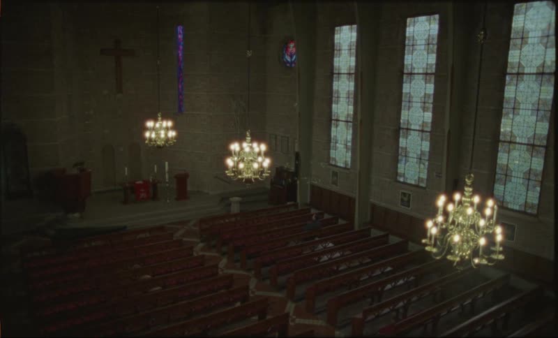 Interior of a church with lit chandeliers and a man sitting on a bench