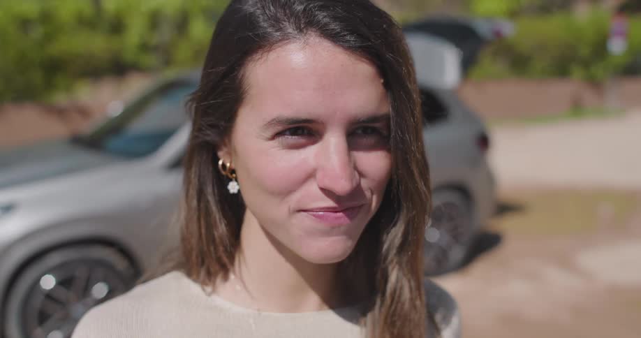 A smiling young woman with long hair standing in front of a parked vehicle