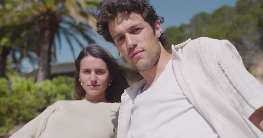 Man and woman side by side wearing a white outfit leaning against the hood of the car posing