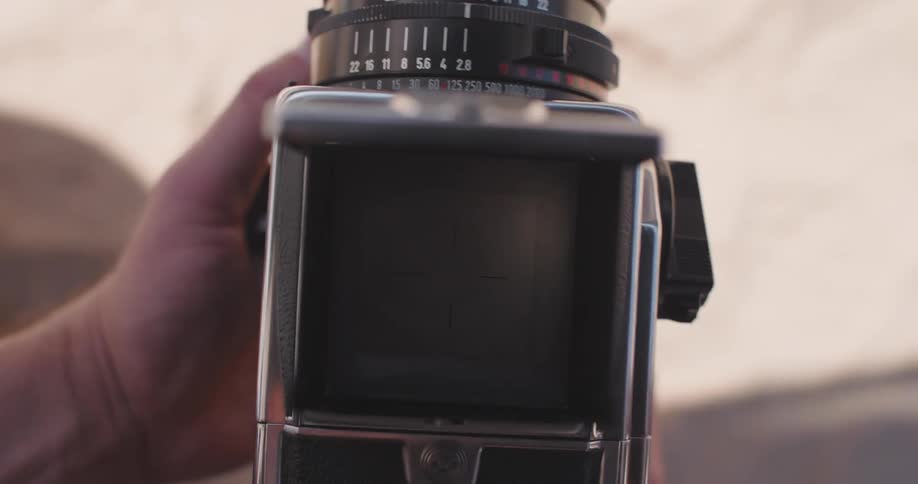 A persons hands holding a camera focused on a woman reading a book in the beach
