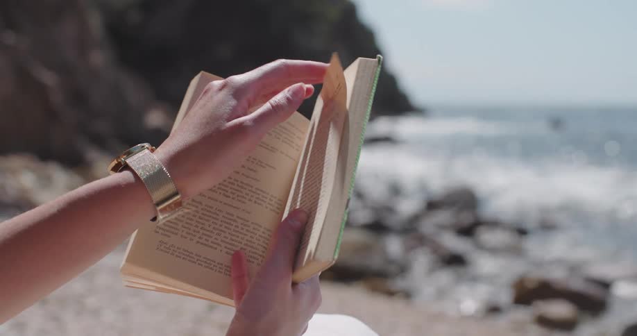A woman is reading a book on the beach