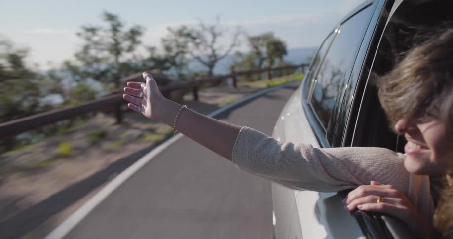 Woman in the front seat with her hand out the window and enjoying the wind of the moving car