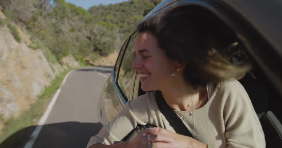Woman in the front passenger seat of a moving car with her arm out enjoying the vibe of the natural environment