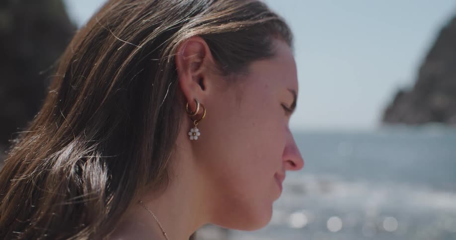 Side portrait of a young woman on the beach wearing a gold flower earring