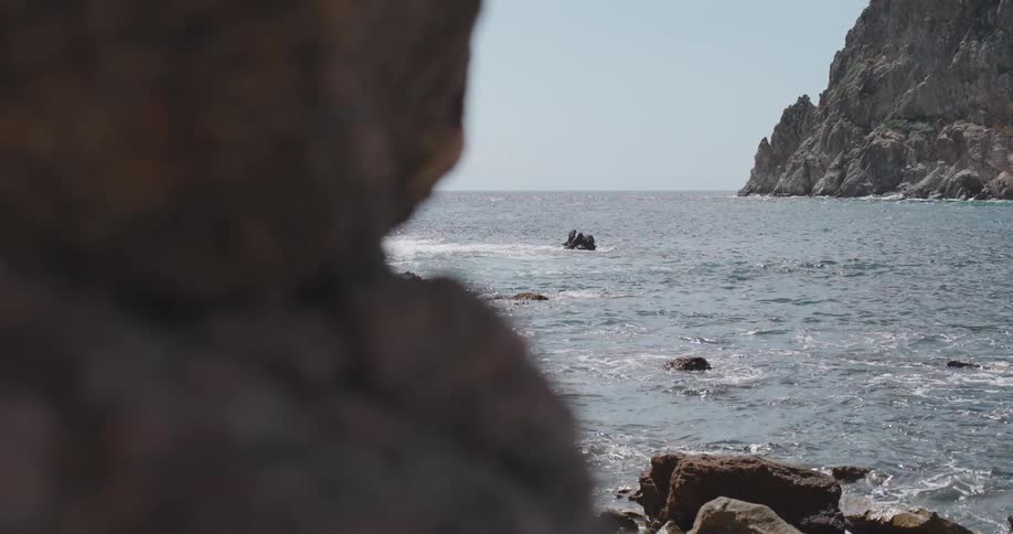 Waves flow over boulders near coast in cove enclosed by mountains