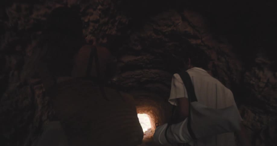 Man and woman with bags going through a cave in a natural environment