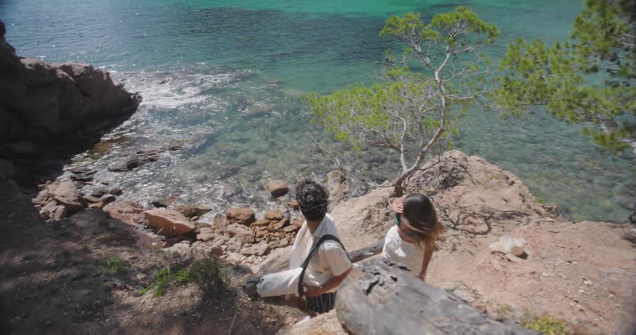 A young couple climbing a rocky slope overlooking a beach