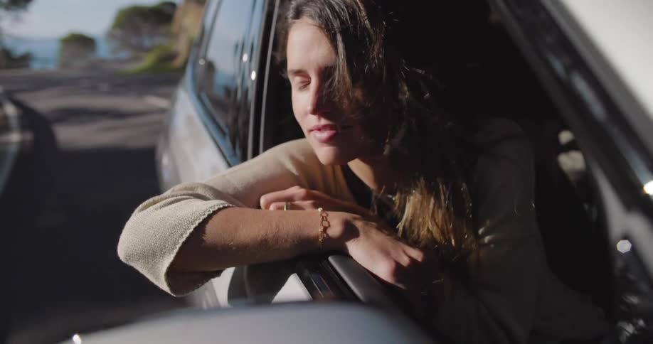 A woman is hanging out the window has she rides in the car