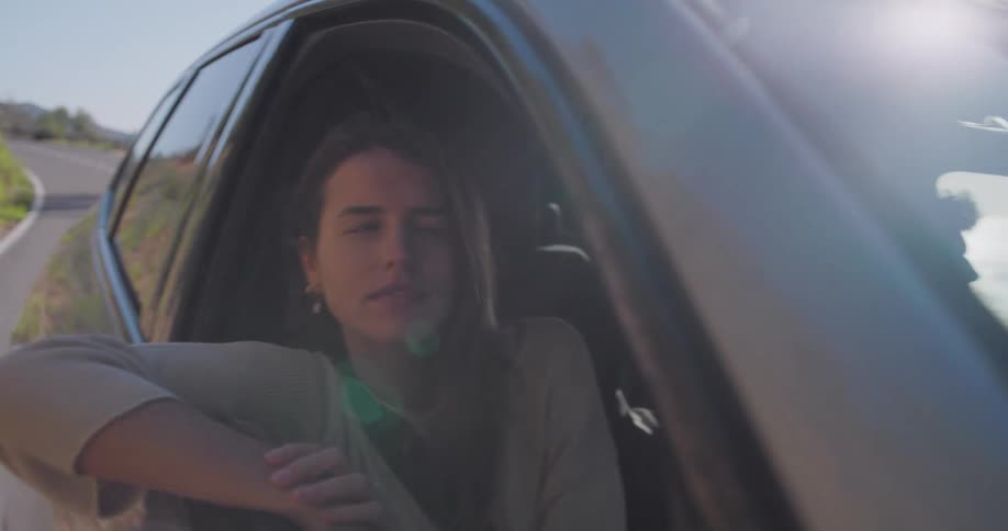 Female passenger leans out window during road trip on a coastal highway
