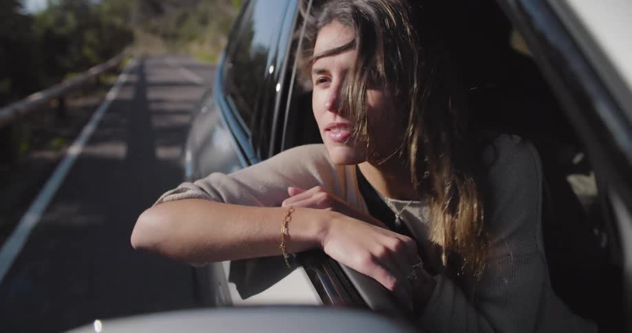 Woman sitting in the front seat with the window down taking a breather on the road in an environment with nature around her